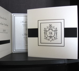 Pearl/matte black foldover has a black satin ribbon running under a 4-layer crested monogram mount, 4 layers inside with invitation print and a clean pearl pocket secured with black satin ribbon for inserts.