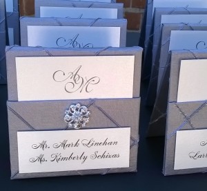 Tented pockets made from silver pintuck fabric, detailed with rhinestone bling, hold a monogram insert with table assignment.