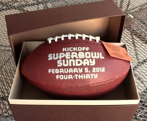 Standard size printed football with custom Louis Vuitton-inspired box, coppery stadium ticket hangs from laces with copper cord, box band closure same color and texture as football