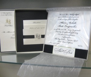 Printed Lucite invitation sits over a dimensional moiré illusion plastic, detailed with a black satin ribbon and name style mounting